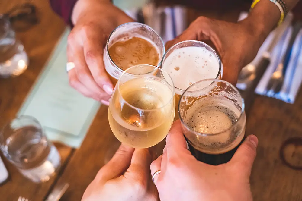 Inselstube Getraenke Vier Hände die Gläser mit Wein und Bier halten, stoßen an